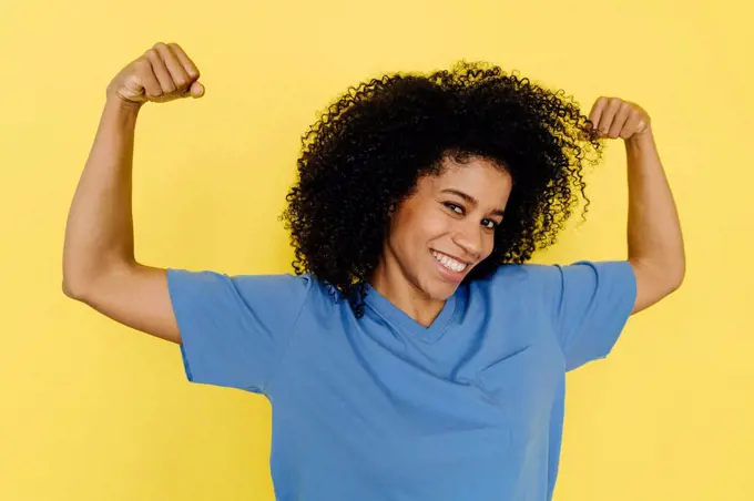 Smiling woman flexing muscles against yellow background