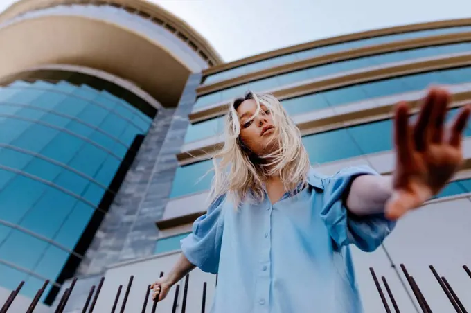 Young blond woman gesturing while standing in front of building