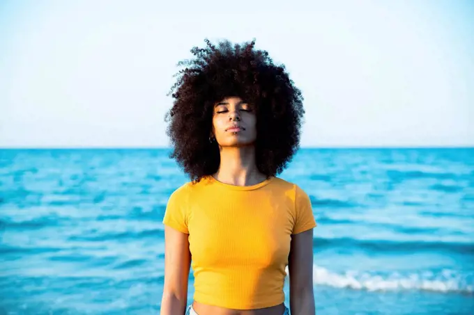 Young Afro woman with eyes closed standing at beach