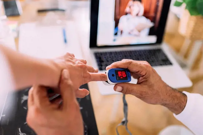 Male doctor examining patient through oximeter during telemedicine in hospital