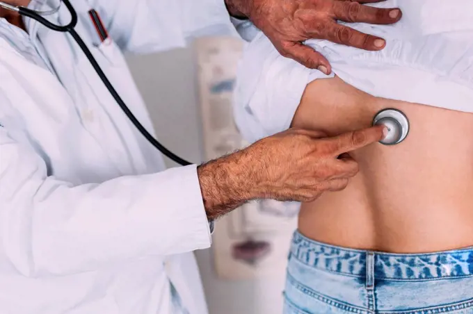 Male doctor checking female patient through stethoscope at clinic