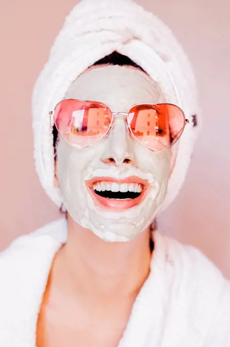 Happy young woman with beauty face mask wearing heart shape sunglasses