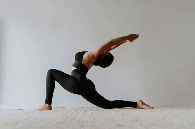 Female fitness teacher with arms raised bending backwards while practicing yoga