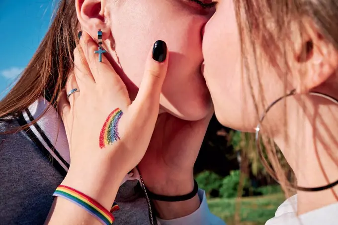 Woman with rainbow wristband and tattoo kissing girlfriend on sunny day