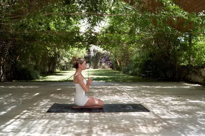 Woman with hand clasped meditating on exercise mat in garden