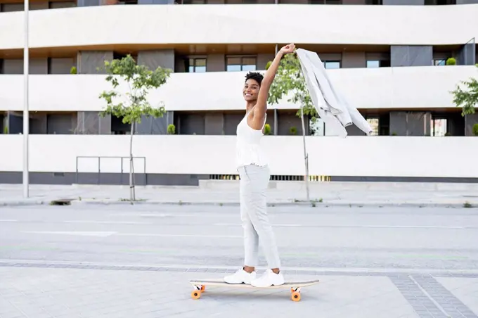 Carefree businesswoman holding blazer while skateboarding in city