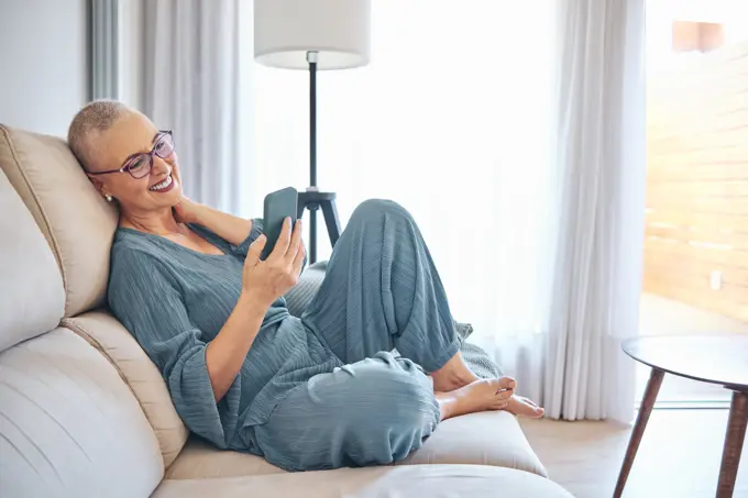 Smiling mature woman using smart phone while sitting on sofa at home