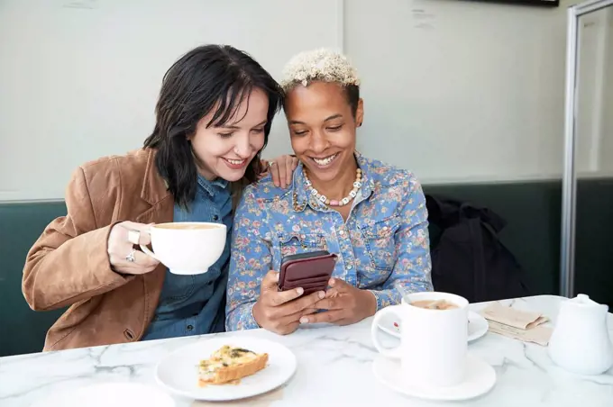 Happy lesbian couple sharing smart phone while sitting in cafe