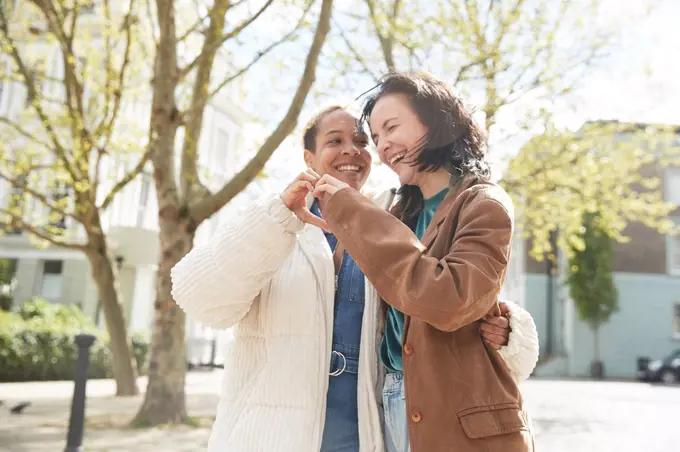 Cheerful woman gesturing heart shape with girlfriend