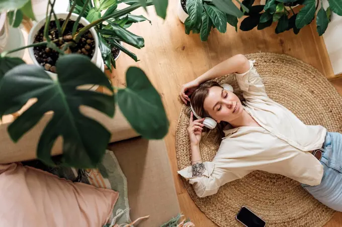 Woman with hands raised listening music while relaxing on rug at home