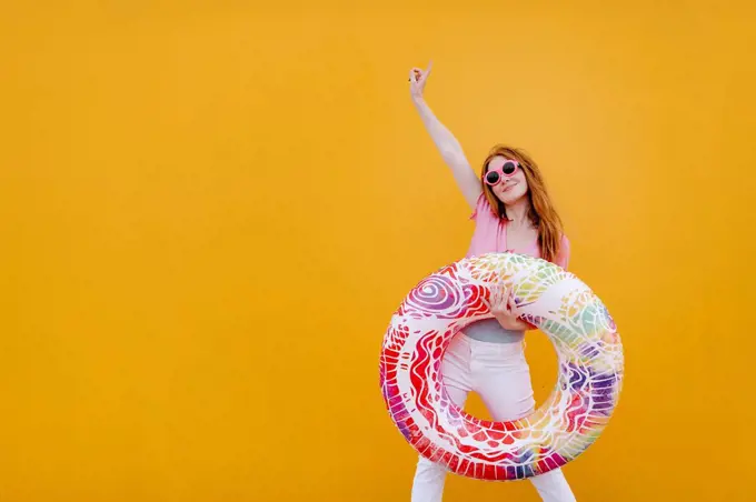 Carefree woman with hand raised holding inflatable ring