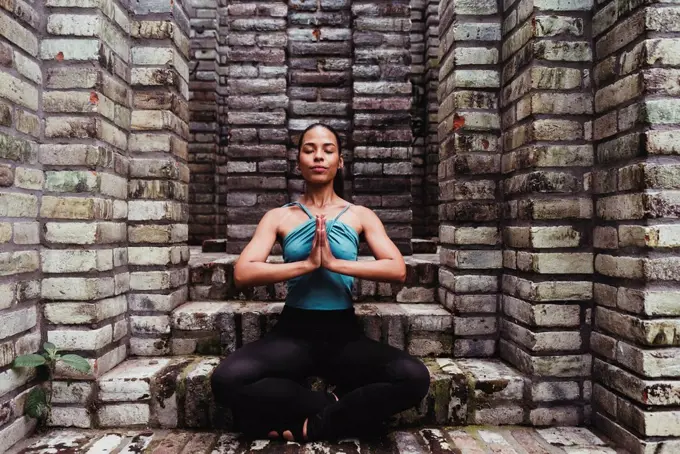 Young woman meditating with hands clasped in stone structure