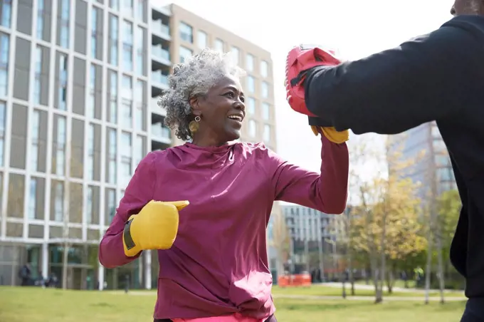 Smiling woman practicing boxing with man at park on sunny day