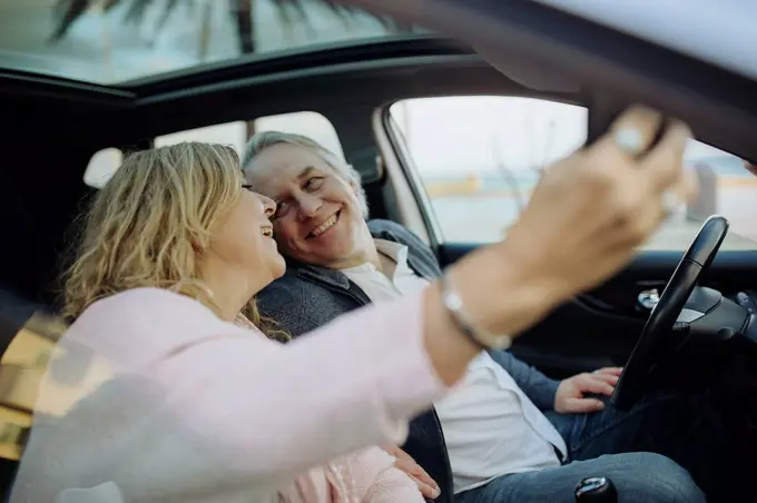 Happy mature couple looking at each other while taking selfie sitting in car