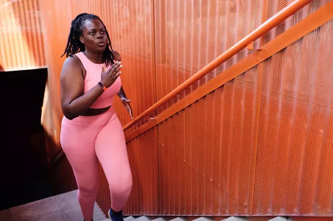 Plus size woman in sports clothing running on staircase