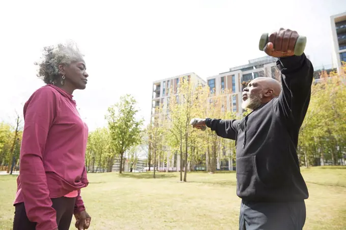 Senior woman looking at man exercising with dumbbells in public park
