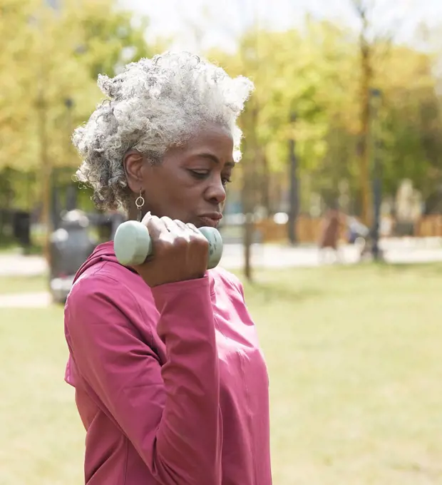 Active senior woman exercising with dumbbell in public park