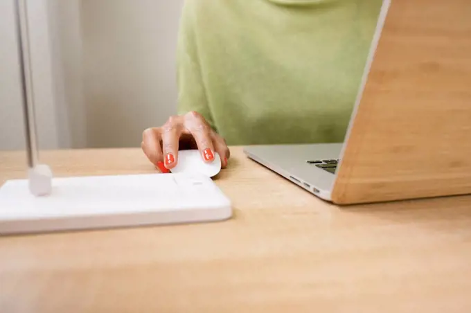 Woman using computer mouse while working on laptop