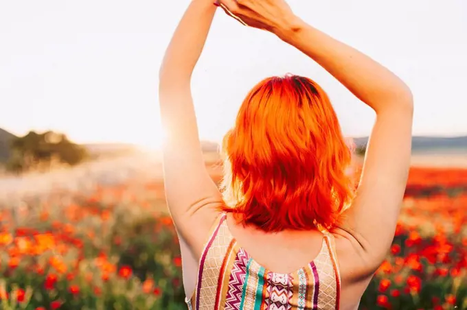 Redheaded woman with hands raised at sunset