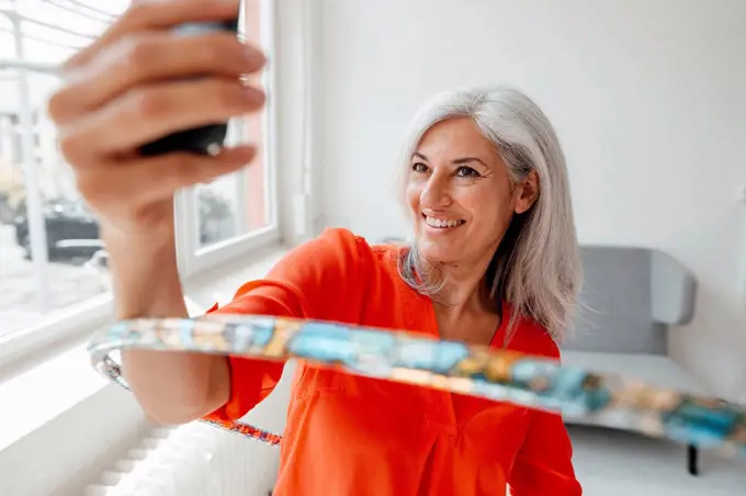 Smiling businesswoman taking selfie through smart phone while practicing with hula hoop at office