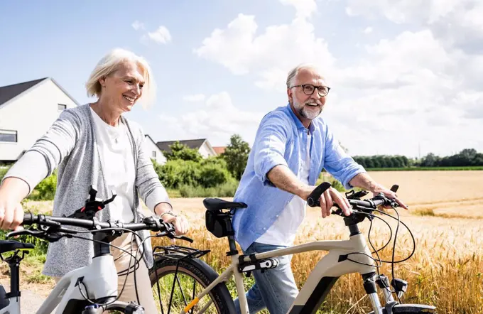 Smiling couple walking with bicycles during sunny day