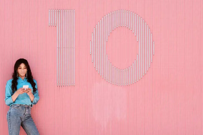 Female transgender using mobile phone by number 10 on pink corrugated wall