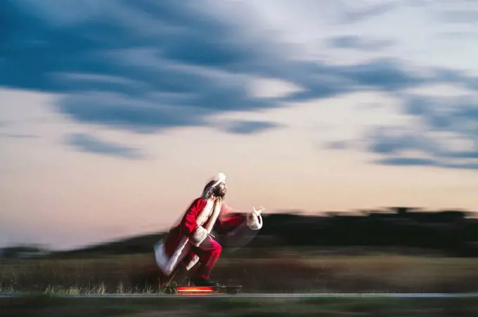 Man skateboarding on road wearing Santa Claus costume at dusk