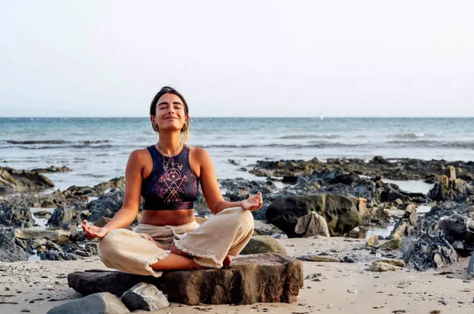 Smiling woman meditating on rock at beach