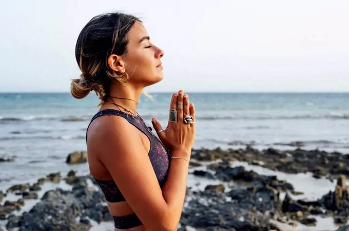 Young woman with hands clasped meditating at beach