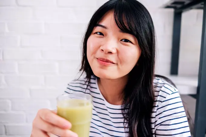 Young woman holding healthy smoothie at home