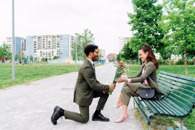 Businessman giving bouquet to colleague while kneeling on footpath