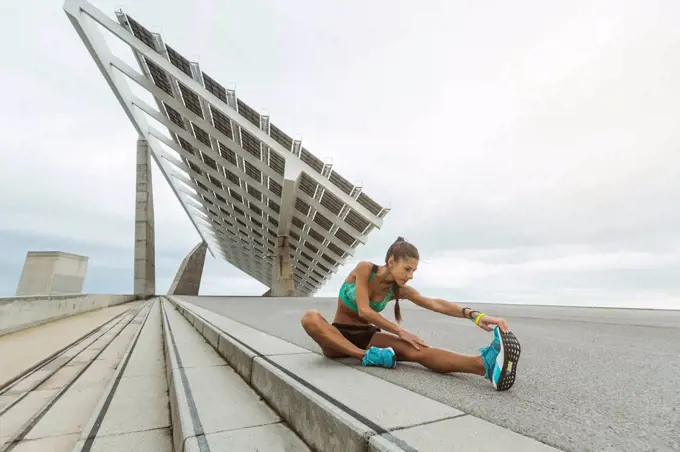 Female athlete stretching legs while sitting on footpath