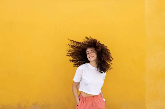 Carefree woman tossing hair in front of yellow wall