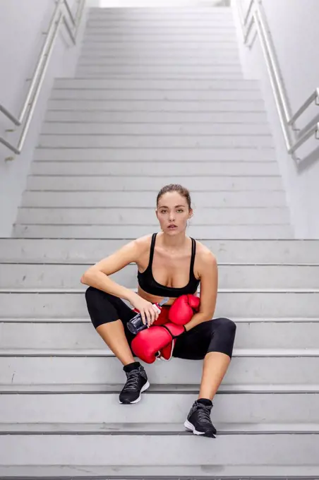 Confident young female athlete sitting on staircase at basement