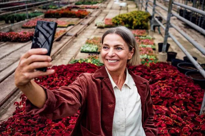 Smiling female farmer taking selfie through smart phone in plant nursery