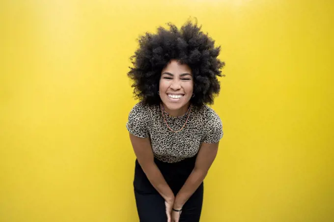 Afro woman smiling in front of yellow wall