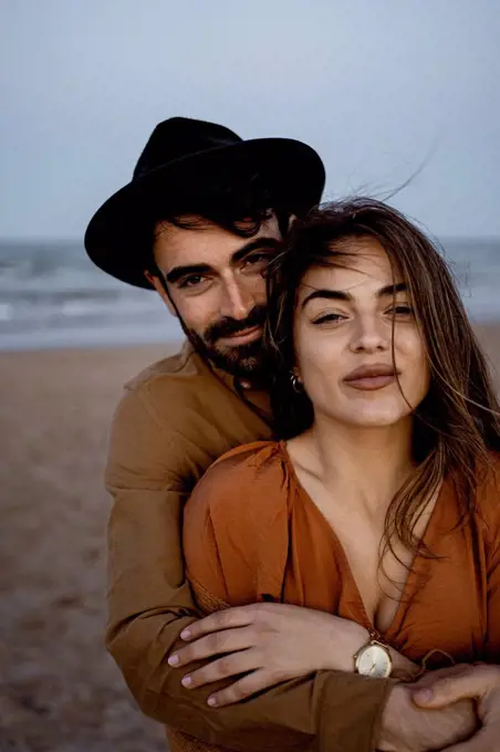 Boyfriend embracing girlfriend from behind at beach during sunset