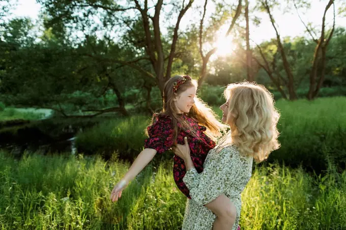 Mother carrying playful daughter during sunset