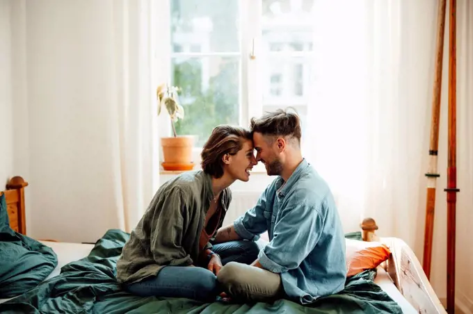 Couple touching foreheads while sitting on bed at home