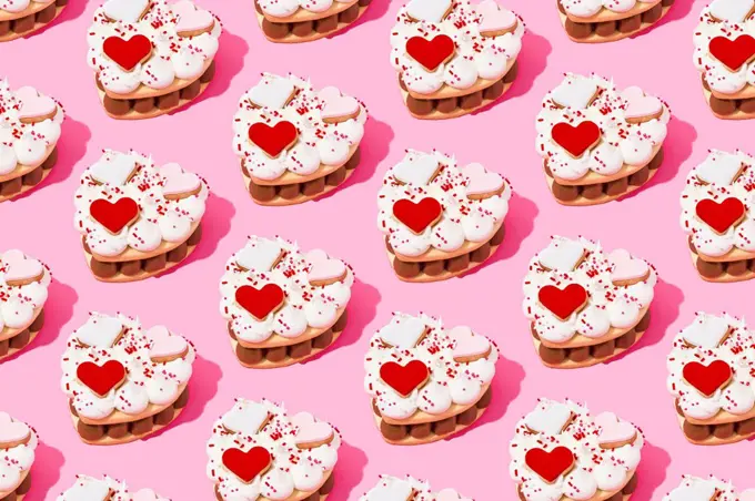 Pattern of heart shaped cookie cakes flat laid against pink background