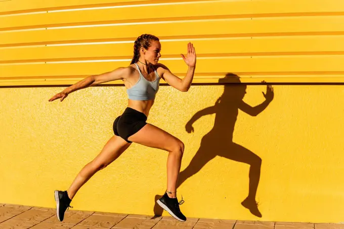 Young female athlete running by yellow wall