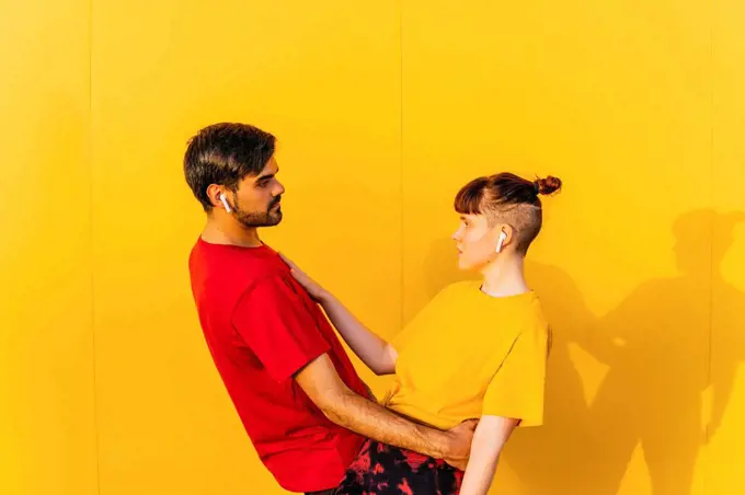 Couple looking at each other while standing by yellow wall