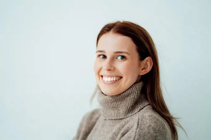 Smiling woman with brown hair by white background