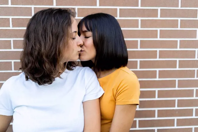 Affectionate lesbian couple kissing in front of brick wall