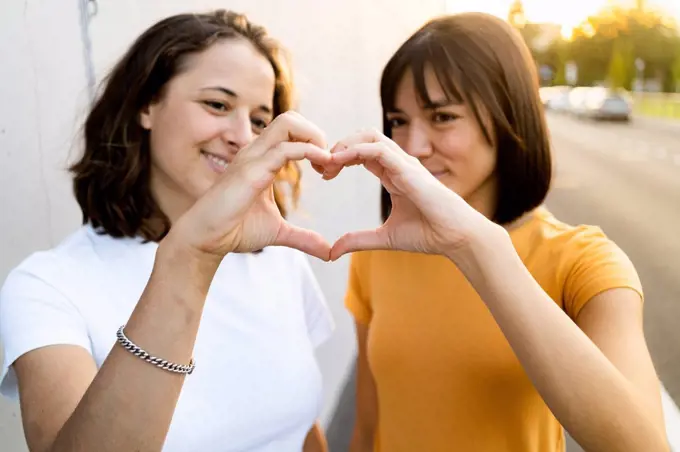 Young lesbian couple making heart with hands during sunset