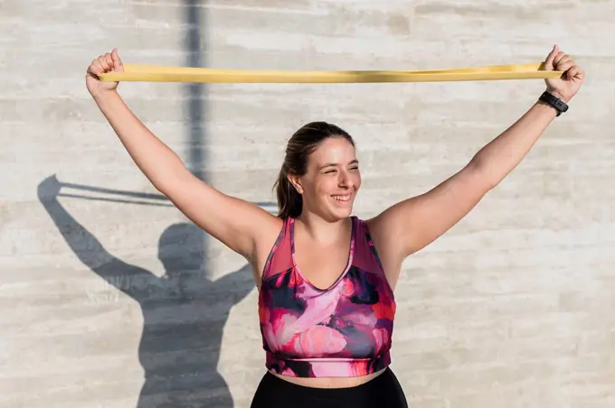 Happy female athlete stretching resistance band while exercising during sunny day