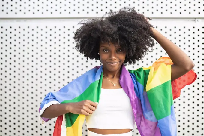 Afro woman wearing pride flag standing in front of metal wall