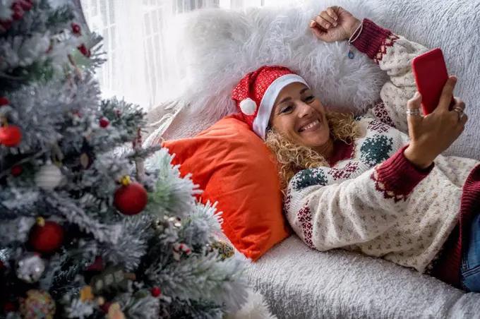 Woman wearing Santa hat taking selfie through smart phone at home