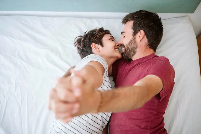 Affectionate couple with hands clasped lying on bed at home