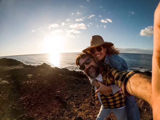 Happy mature man giving piggyback ride to woman while standing in front of sea